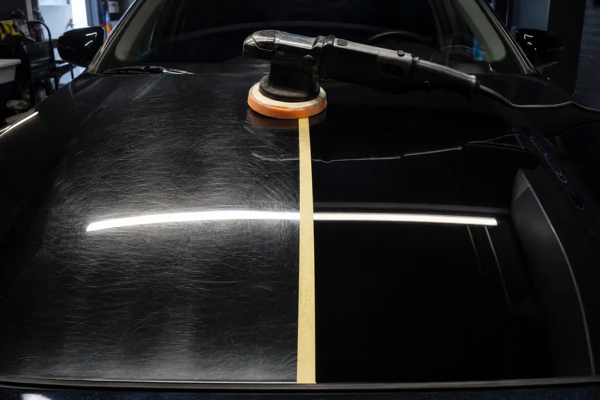 Dual-action polisher resting on a half-corrected hood, swirled paint on one side and clear gloss on the other, in Austin, TX