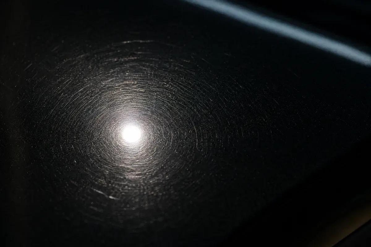 Spiderweb swirl marks showing under a swirl-finder light on dark paint before paint correction